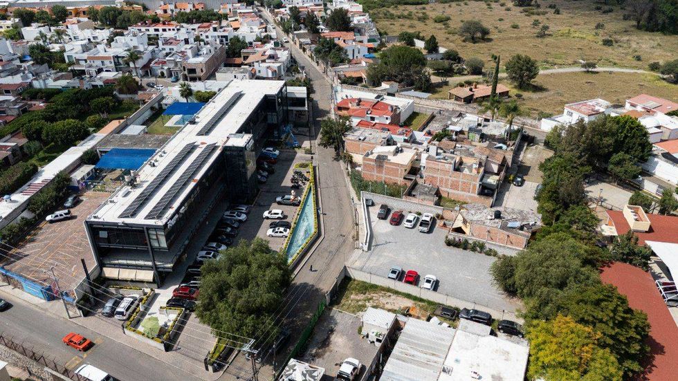 Vista a\u00e9rea de una calle y viviendas junto a un edificio grande de techo blanco con equipos de enfriamiento.