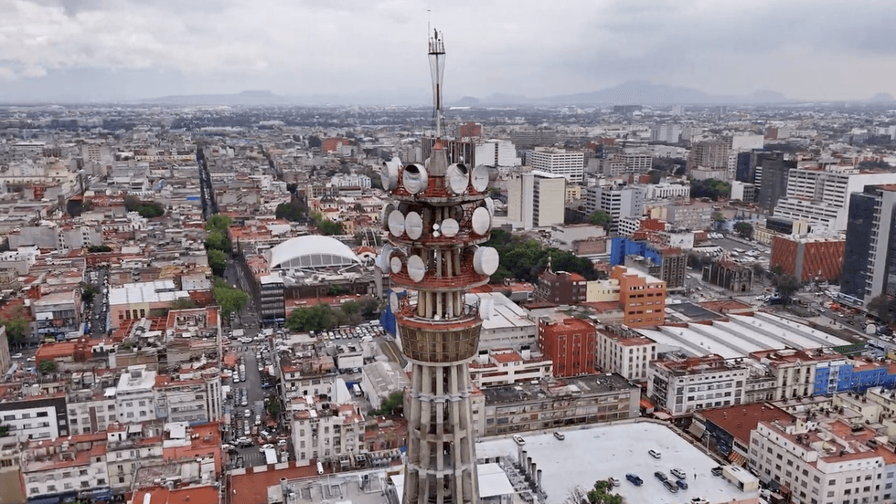 Vista a\u00e9rea de una torre de microondas con antenas parab\u00f3licas sobre una extensa zona urbana, con monta\u00f1as al fondo, en una nota sobre la licitaci\u00f3n de espectro de la CRT para internet rural