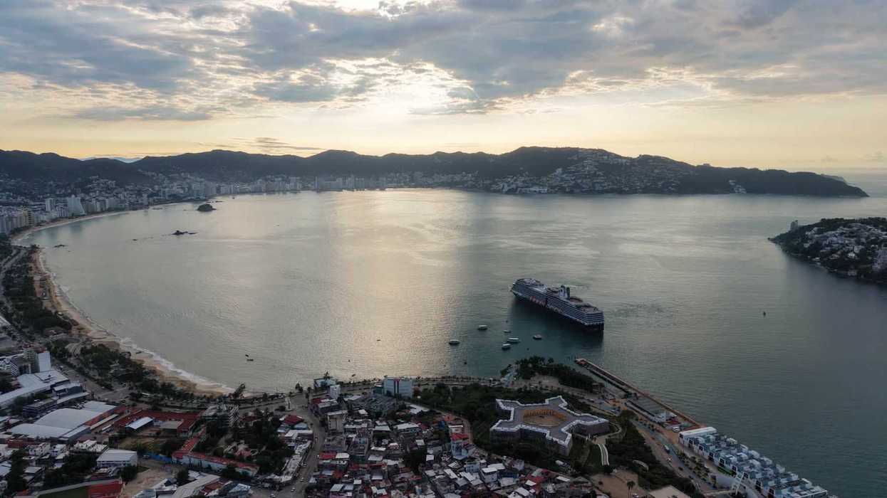 Vista aérea al atardecer de una bahía con un crucero y un fuerte de forma estrellada en primer plano, bajo un cielo nublado.