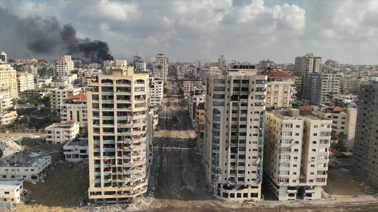 Vista aérea de edificios de varios pisos dañados a ambos lados de una avenida cubierta de escombros en Gaza, con una columna de humo al fondo