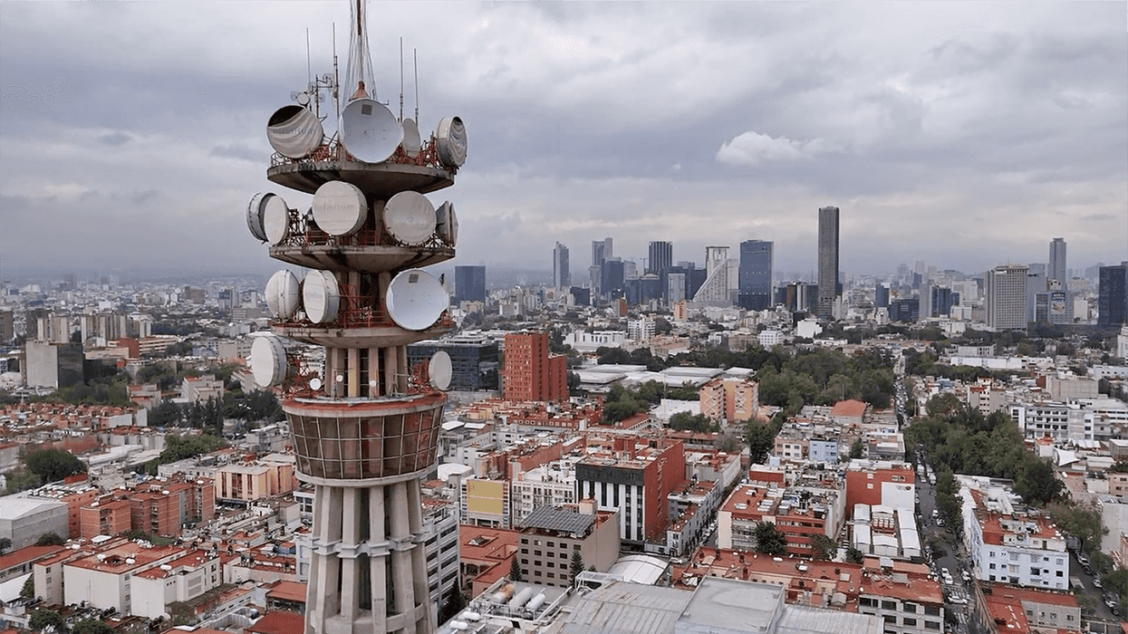 Vista aérea de una torre de microondas con antenas parabólicas sobre una extensa zona urbana, con montañas al fondo, en una nota sobre la licitación de espectro de la CRT para internet rural