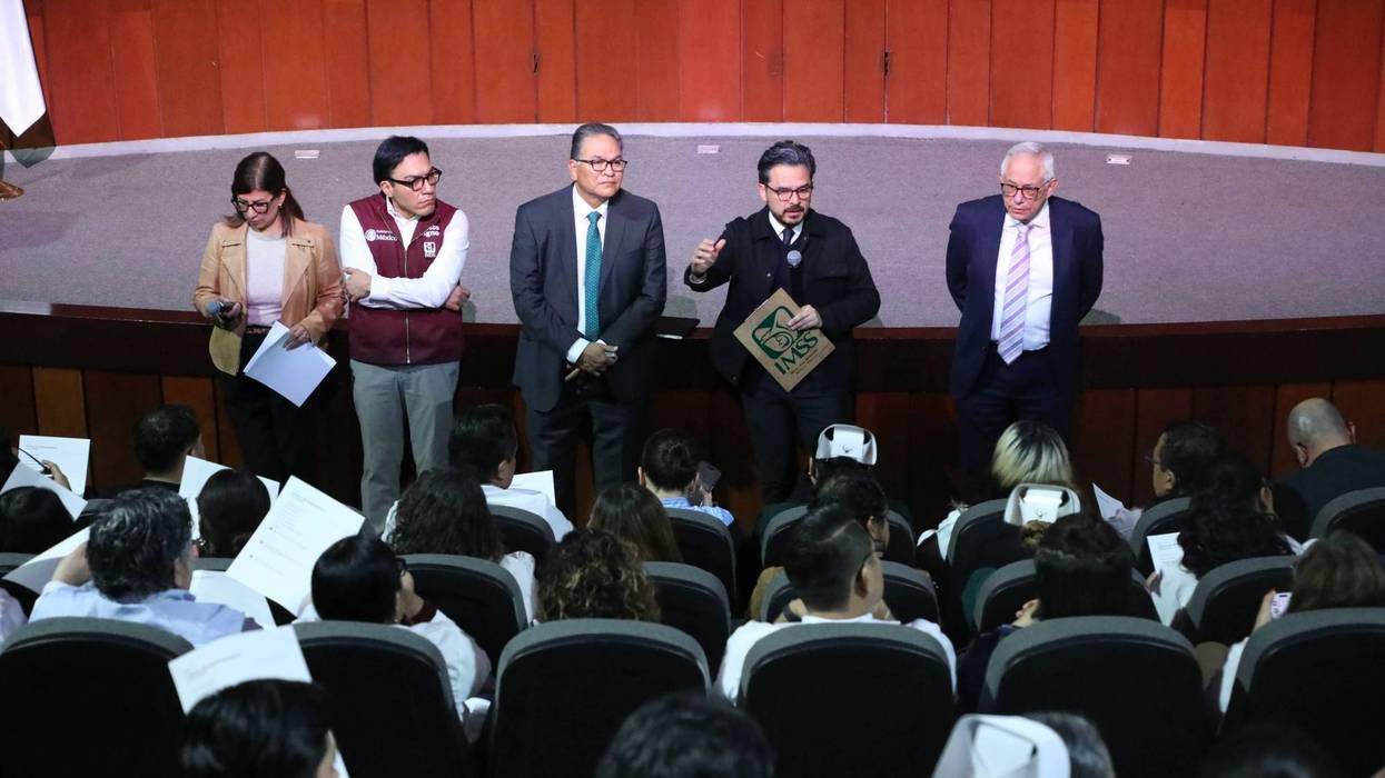 Vista del auditorio de la CISS con asistentes con batas y cofias de enfermería frente a un escenario con banderas