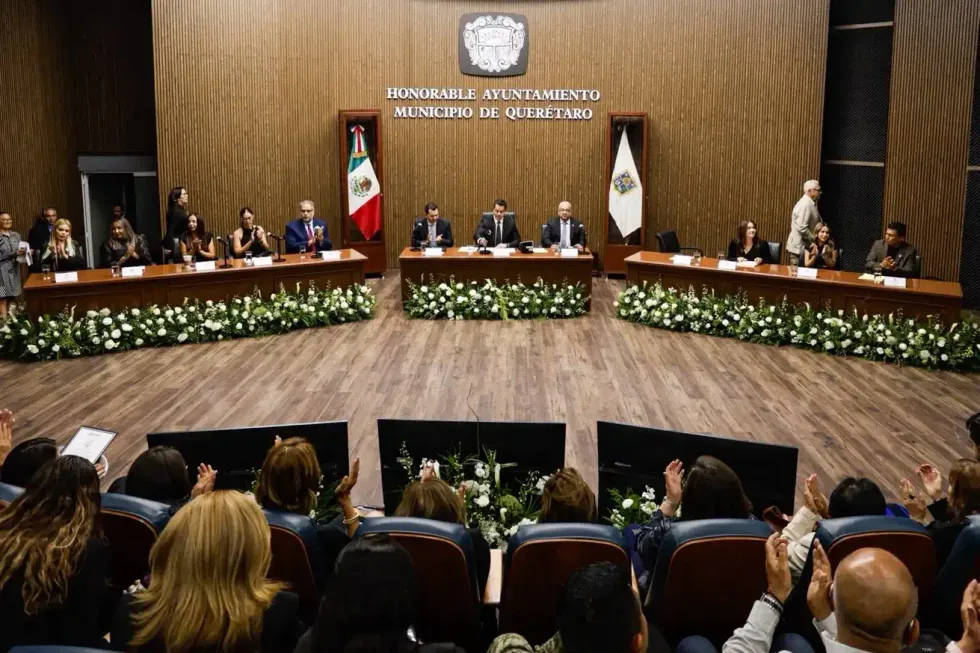 Vista general del sal\u00f3n de sesiones del Ayuntamiento de Quer\u00e9taro durante la sesi\u00f3n solemne, con el pres\u00eddium al frente y asistentes aplaudiendo.