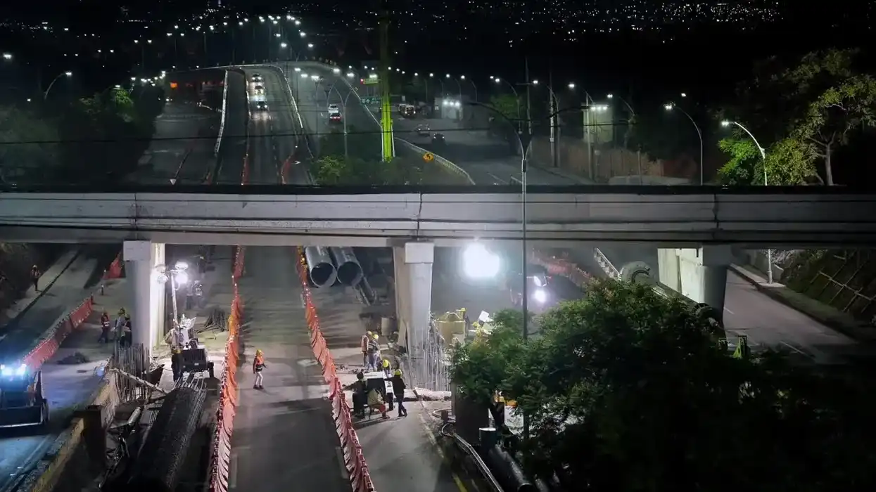 Vista nocturna de la obra federal del Tren México-Querétaro en Bernardo Quintana, con trabajadores bajo el puente y vehículos circulando en el nivel superior