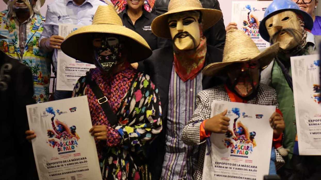 Xhitas con máscaras de palo y trajes de colores sostienen carteles del Festival de la Máscara de Palo